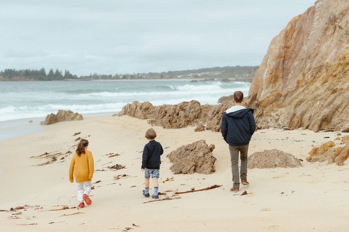 A parent and two children walking on an Australian beach